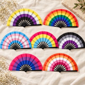 Può includere: Sette ventagli pieghevoli con stecche in plastica nera, ognuno con un diverso motivo di bandiera dell'orgoglio. I design includono gli schemi di colore delle bandiere non binaria, arcobaleno, transgender, pansessuale, asessuale, bisessuale e lesbica.