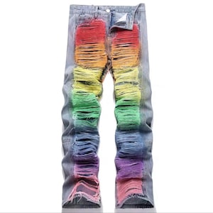 Op de afbeelding: Lichtblauwe spijkerbroek met een opvallend regenboogkleurig distressed patroon over de voorkant van beide broekspijpen. De stof is zwaar gerafeld en gescheurd, waardoor lagen van rode, oranje, gele, groene, blauwe en paarse tinten zichtbaar zijn.