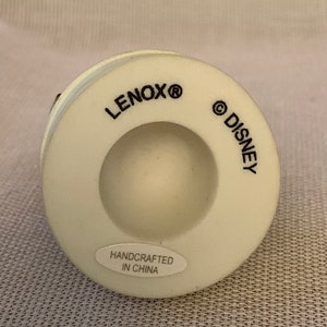 May include: White ceramic figurine base with the words "LENOX&reg;" and "&copy;DISNEY" printed on the bottom. The base also has a sticker that reads "HANDCRAFTED IN CHINA".