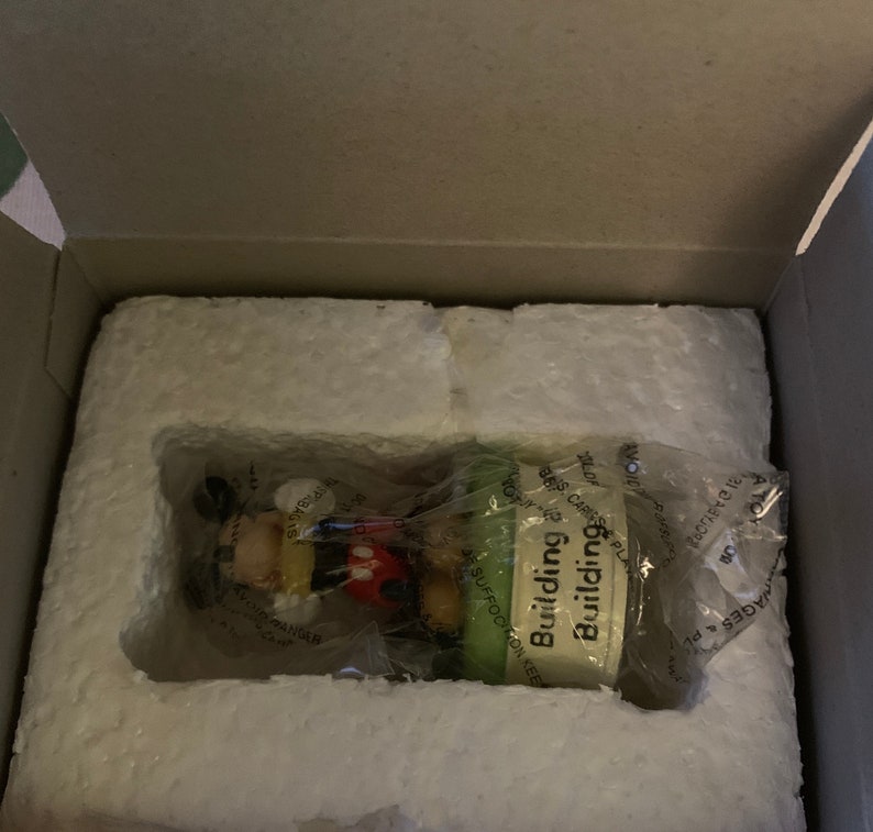 May include: A small, green and white figurine of Mickey Mouse building a house. The figurine is packaged in a white styrofoam box with the words "Building Building" on the front.