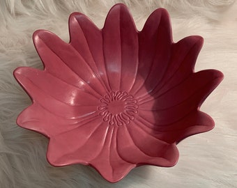 May include: A pink ceramic bowl shaped like a flower with a raised center design.