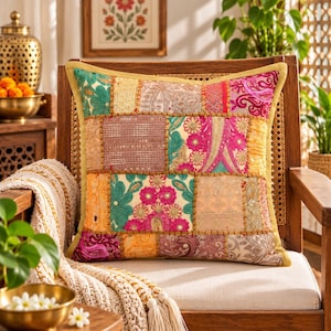 May include: A square throw pillow featuring a patchwork design of various fabric squares in shades of pink, teal, gold, and beige. The fabric panels are embellished with intricate embroidery, sequins, and metallic thread accents, all framed by a solid gold border.