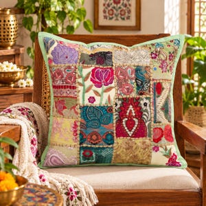 Peut inclure: Un coussin carré présentant un motif patchwork composé de divers tissus brodés dans des tons de rose, rouge, bleu, vert et jaune. Le coussin est bordé d'une bordure vert clair avec des coutures décoratives visibles entre les panneaux.