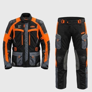 Può includere: Un completo da moto composto da giacca e pantaloni neri, grigi e arancioni. La giacca presenta il logo KTM, la scritta READY TO RACE e ADVENTURE. I pantaloni includono tasche cargo laterali, protezioni per le ginocchia e il logo KTM.