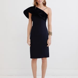 May include: A black one-shoulder dress with a velvet trim detail. The dress has a fitted silhouette and a midi length. The model is wearing black heels.