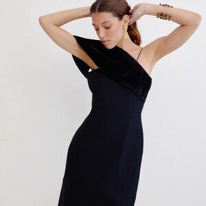 May include: A black one-shoulder dress with a velvet trim on the shoulder strap. The dress is fitted and has a midi length.