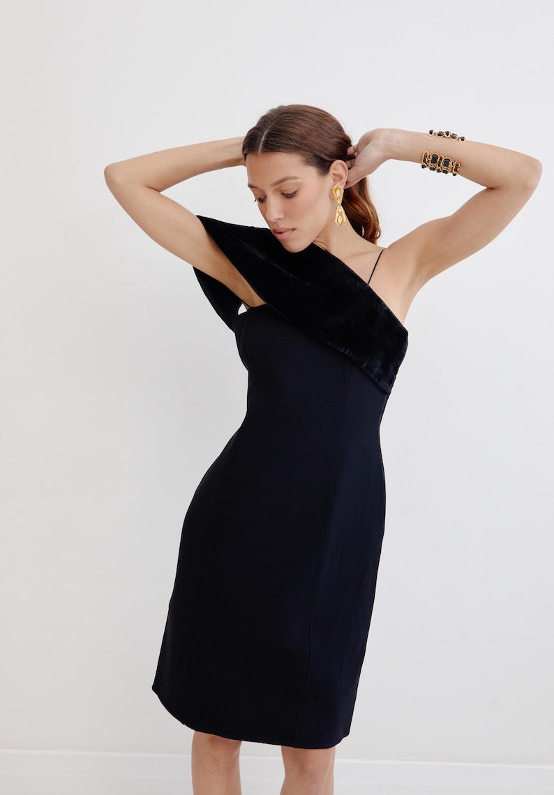 May include: A black one-shoulder dress with a velvet trim on the shoulder strap. The dress is fitted and has a midi length.