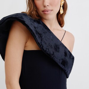 May include: A black one-shoulder dress with a velvet detail on the shoulder. The dress has a fitted silhouette and a simple design.
