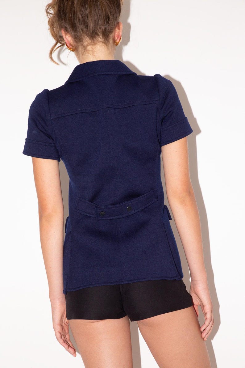 K&ouml;nnte beinhalten: Marineblaue Jacke mit kurzen &Auml;rmeln, Hemdkragen und taillierter Passform. Die Jacke hat einen Knopfverschluss und ein strukturiertes Design. Das Model tr&auml;gt schwarze Shorts. Diese Jacke ist eine stilvolle Erg&auml;nzung f&uuml;r jede Garderobe.