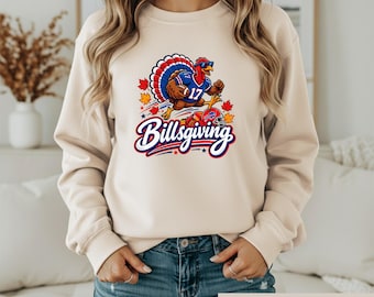 May include: A sand-colored crewneck sweatshirt featuring a graphic of a turkey wearing sunglasses and a football jersey with the number 17, holding a football. The text Billsgiving is printed below in blue and red, surrounded by autumn leaves.
