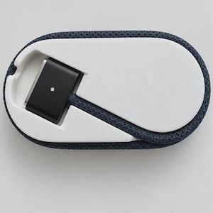 Op de afbeelding: Een marineblauwe gevlochten oplaadkabel gewikkeld rond een witte, ovaalvormige plastic spoel. De kabel is voorzien van een zwarte magnetische connector aan het ene uiteinde en een witte USB-C-connector aan het andere uiteinde.
