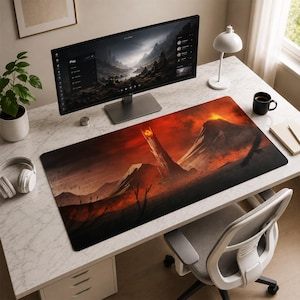 May include: A rectangular desk mat featuring a high-contrast illustration of a dark, towering fortress with a glowing orange eye at its peak, set against a fiery, volcanic landscape with deep red and black tones, positioned on a white marble desk.