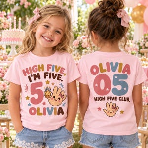 May include: A light pink short-sleeved t-shirt featuring a graphic print. The front displays the text "HIGH FIVE, I'M FIVE," the number "5," a cartoon hand, and the name "OLIVIA." The back shows "OLIVIA," the number "05," and "HIGH FIVE CLUB."