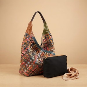Puede incluir: Un bolso hobo con un patrón de cuero trenzado multicolor en tonos rojo, naranja, marrón y verde, con correas de cuero marrón y verde. Junto a él hay un estuche rectangular negro liso y un pañuelo de seda de color beige claro doblado.