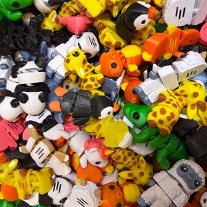 May include: A large collection of small, articulated plastic animal figures in various colors including yellow, orange, green, black, and white. The assortment features miniature giraffes, pandas, penguins, pigs, and other creatures with segmented bodies.