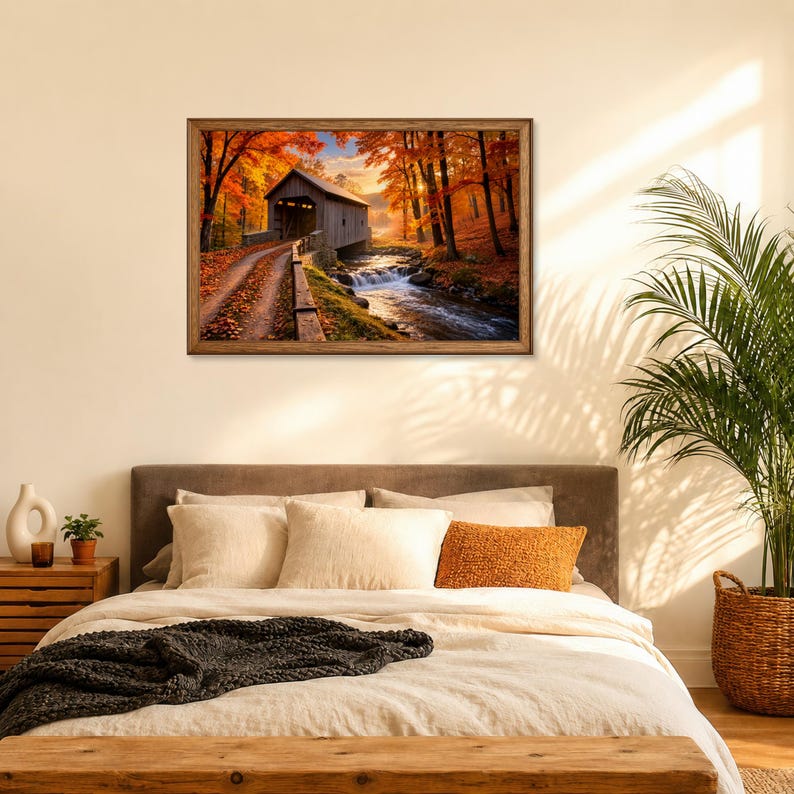 Op de afbeelding: Een rechthoekige ingelijste wandkunstprint met een houten overdekte brug over een stromende beek in een herfstbos. De sc&egrave;ne toont levendig oranje en geel gebladerte, een onverhard pad bedekt met bladeren en zacht zonlicht.
