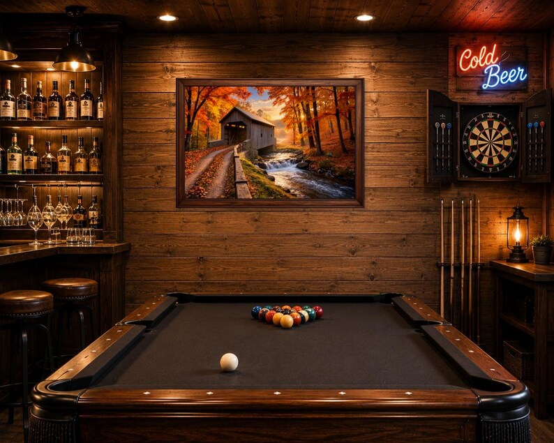 Op de afbeelding: Een speelkamer met een donkerhouten pooltafel, een dartbord aan de muur met een neon Cold Beer-bord, een bar met planken vol glazen flessen en een ingelijst landschapsschilderij van een overdekte brug in een herfstachtig landschap.