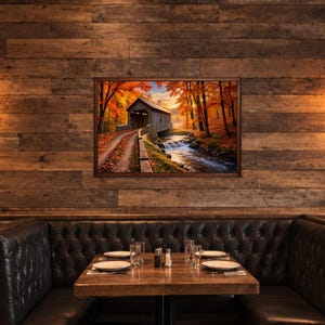 Op de afbeelding: Een rechthoekige ingelijste wandkunstprint met een overdekte brug over een stromende beek, omringd door herfstbomen met levendig oranje en geel gebladerte. De sc&egrave;ne toont een zandpad dat in het herfstseizoen naar de brug leidt.