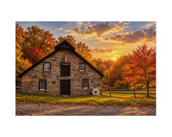 May include: A stone building labeled The Old Mill with a dark wooden door and windows, featuring an American flag hanging above the entrance. The structure is surrounded by autumn trees with orange and yellow foliage under a sunset sky.