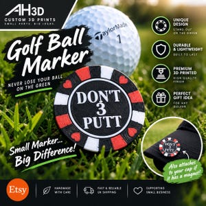 May include: A round, black, white, and red golf ball marker featuring the text DON'T 3 PUTT in white lettering. The marker has a poker chip design with heart symbols and is shown next to a white golf ball and attached to a black cap.