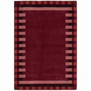 May include: A rectangular area rug featuring a solid deep burgundy center. The border consists of alternating blocks of dark maroon, light pink, and burnt orange, creating a structured geometric frame around the central field.