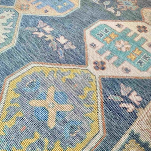 Könnte beinhalten: Ein gewebter Teppich mit einem sich wiederholenden geometrischen Muster aus miteinander verbundenen Sechsecken in den Farben Dunkelblau, Türkis, Senfgelb und Creme. Das Design enthält komplexe florale und abstrakte Motive.