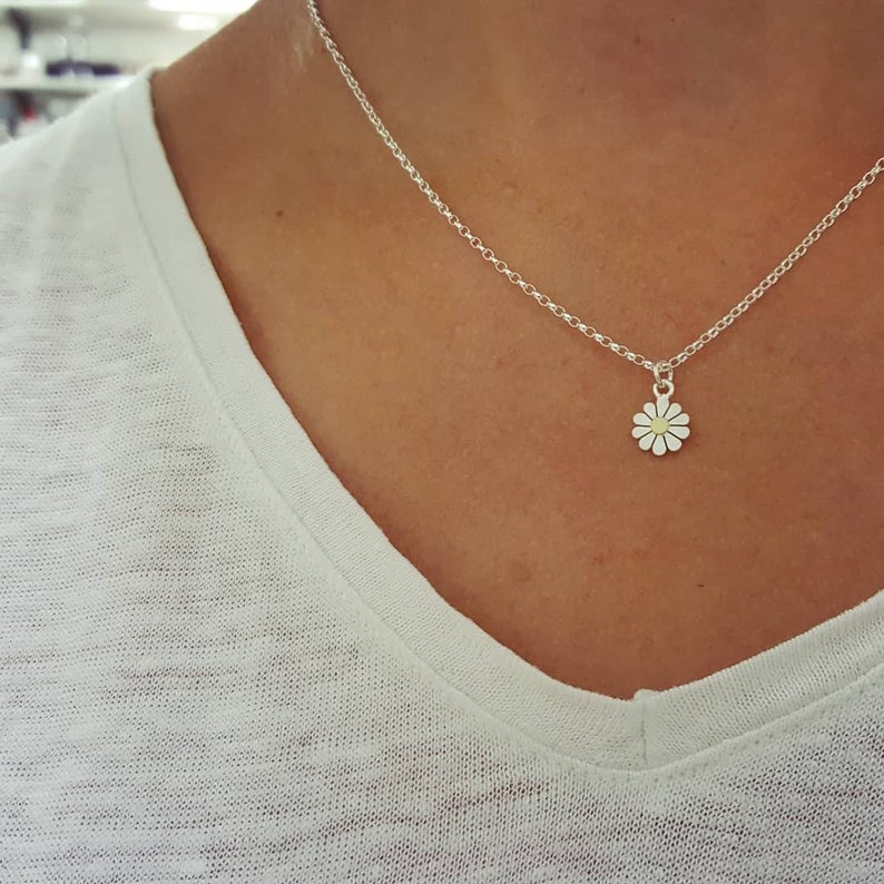 A silver chain necklace with a small silver daisy pendant.