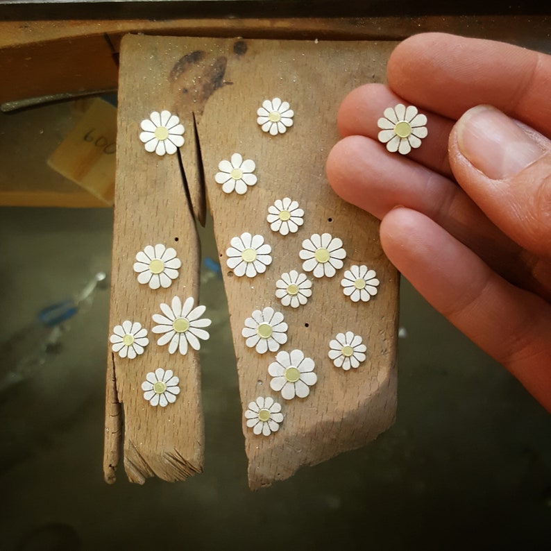 A jewellers benchpeg with small silver daisies with gold centers on top.