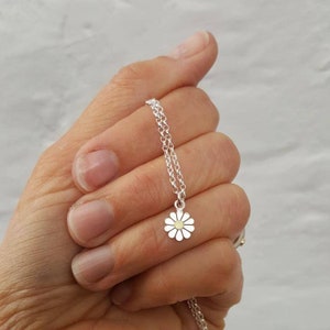 A silver chain necklace with a small silver daisy pendant. The daisy has a yellow gold center and silver petals.