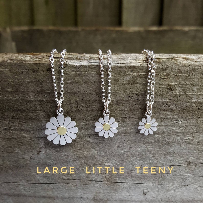 Three silver necklaces with daisy pendants. The daisies are silver with a gold center. The necklaces are arranged from left to right in order of size: large, little, teeny. The text below the necklaces reads: 'LARGE LITTLE TEENY'.
