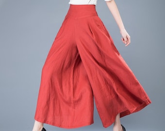 Pode incluir: Uma mulher vestindo uma blusa branca e calças largas de linho vermelho. Ela está em pé com as pernas ligeiramente afastadas e os braços ao lado do corpo.