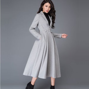 May include: A light gray, knee-length coat with a tailored blazer-style top and a flared skirt. The coat features a two-button closure, long sleeves, and pockets. The model is wearing black ankle boots.