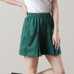 May include: A person wearing a white crew neck t-shirt and green shorts with pockets. The shorts have an elastic waistband. The person is wearing black platform sandals. The outfit is casual and comfortable.