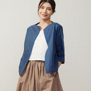 May include: A woman wearing a blue denim jacket over a white t-shirt and a brown midi skirt. She is standing on a tiled floor and wearing brown sandals.