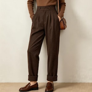 May include: A brown turtleneck sweater, dark brown high-waisted trousers with button details and pleats, a brown fedora hat, and a small brown shoulder bag. The outfit is completed with dark brown loafers, creating a coordinated monochromatic look.