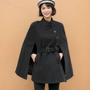 May include: A black cape with a belt and buttons, worn over black trousers and boots. The person is wearing a white and black hat.