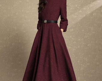 May include: A burgundy-colored dress with long sleeves and a flared skirt. The dress features a black belt and is paired with black heels. The dress has a classic, elegant design, suitable for formal occasions.