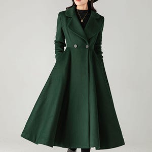 May include: A long, forest green coat with a double-breasted design and a flared skirt. The coat features a notched collar, two rows of buttons, and pockets. The person in the image is wearing a black hat and boots.