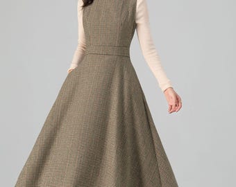Puede incluir: Un vestido sin mangas a cuadros marrones y beige con un corpiño ajustado y una falda acampanada. El vestido se combina con un cuello alto beige y zapatos marrones. El vestido tiene un estilo clásico y elegante.