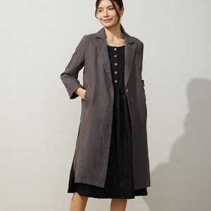 May include: A gray linen blazer with a long, relaxed fit and a single button closure. The blazer has two pockets and is worn over a black dress.
