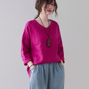 May include: A woman wearing a magenta V-neck long-sleeve shirt and light blue denim pants. The pants have an elastic waistband and are cuffed at the ankles. She is also wearing a necklace and brown shoes.