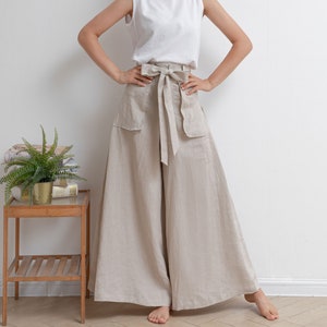May include: A woman wearing a white sleeveless top and beige linen wide-leg pants with a matching fabric belt tied in a bow at the waist.