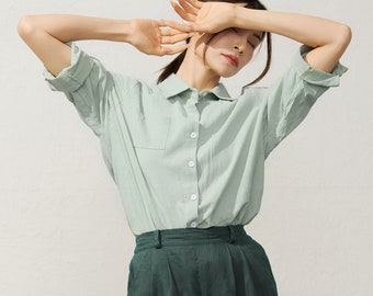 May include: A woman wearing a light green collared shirt with a chest pocket and dark green high-waisted trousers.