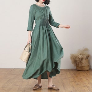 May include: A green linen dress with a gathered waist and a slightly flared skirt. The dress has 3/4 sleeves and a round neckline.