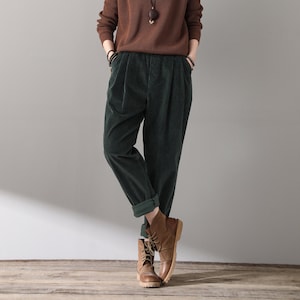 May include: A woman wearing a brown sweater and green corduroy pants. She is wearing brown leather boots and has a necklace with a wooden pendant.