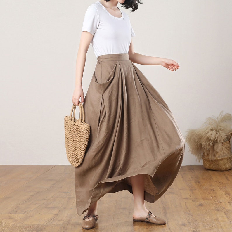 May include: A brown linen maxi skirt with a high waist and a large pocket on the front. The skirt is flowing and has a relaxed fit.