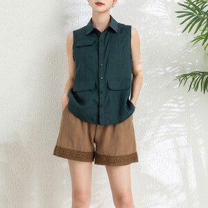 May include: A sleeveless green linen shirt with a button-up front and two flap pockets. The shirt is paired with brown linen shorts that have a lace trim.