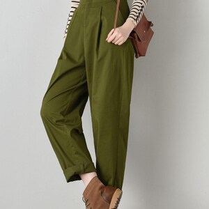 Op de afbeelding: Een olijfgroene broek met hoge taille, een knoopsluiting en plooien. De broek is aan de onderkant gezoomd en het model draagt ​​bruine leren laarzen.