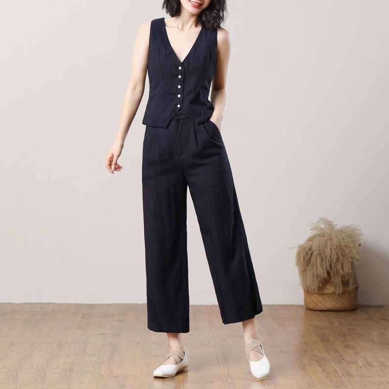 May include: A black sleeveless waistcoat with a button-up front and matching wide-leg trousers. The outfit is made of a linen-like fabric.
