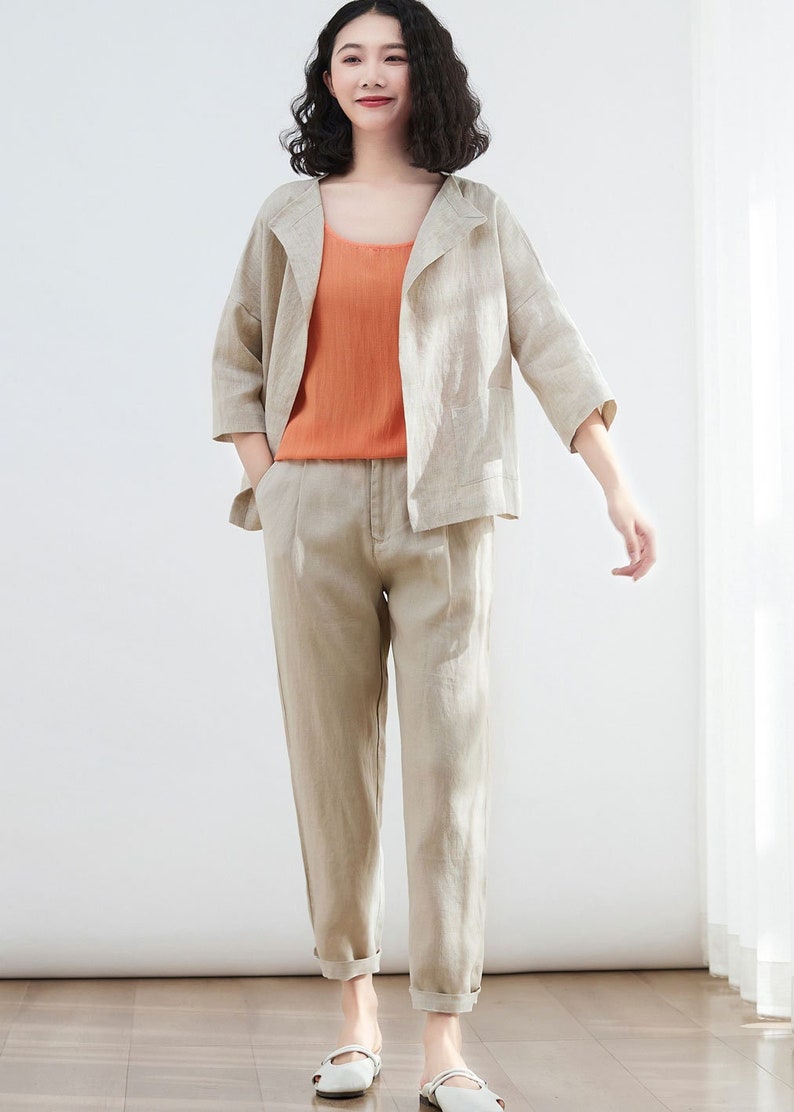 Pode incluir: Uma jaqueta de linho bege com um caimento relaxado e um comprimento ligeiramente curto. A jaqueta tem um colar de xale e mangas tr&ecirc;s quartos. A modelo tamb&eacute;m est&aacute; usando uma cal&ccedil;a de linho bege combinando com perna reta e bainha dobrada.